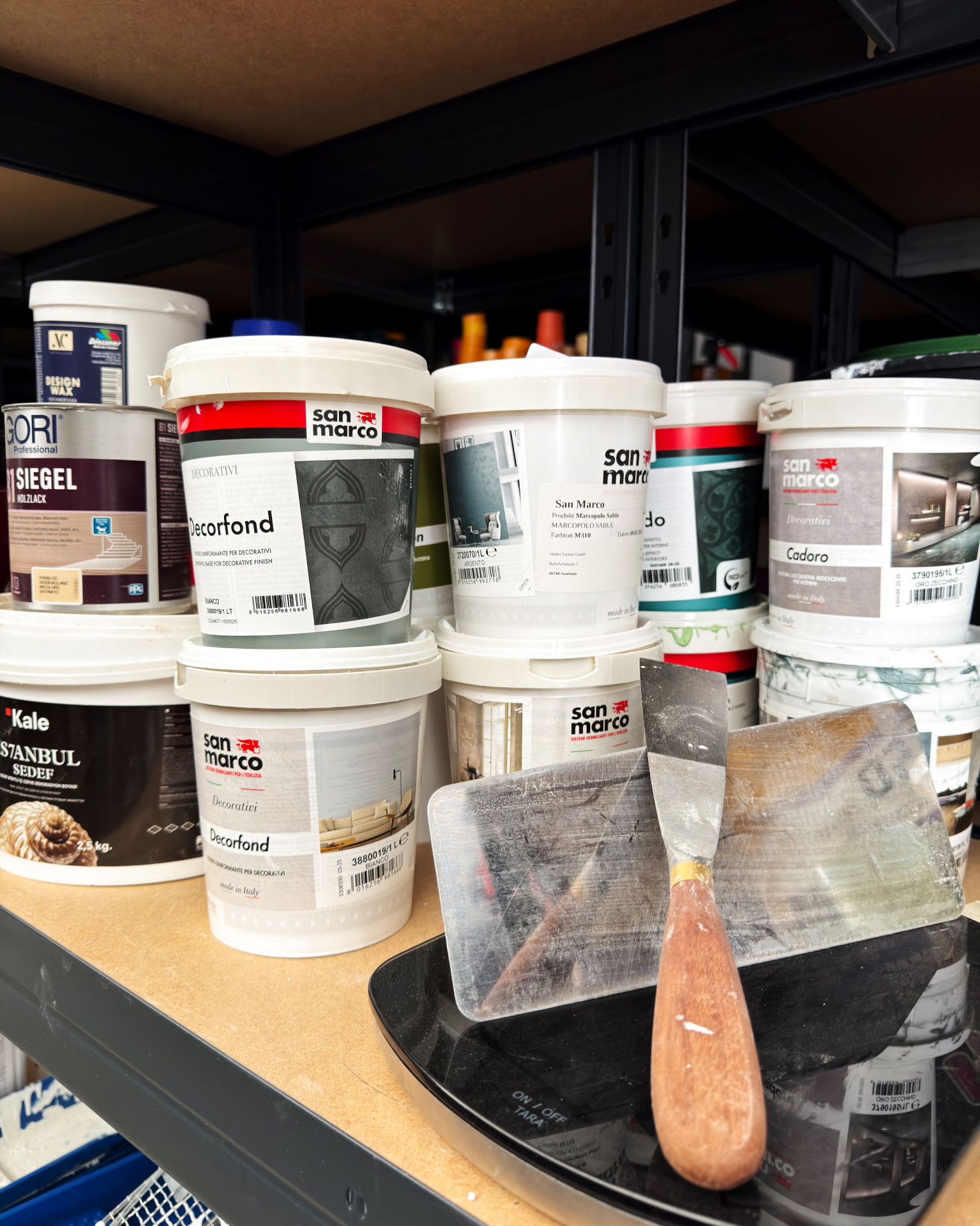 Farbeimer und dekorative Materialien im Regal der Malerwerkstatt Mergenthaler