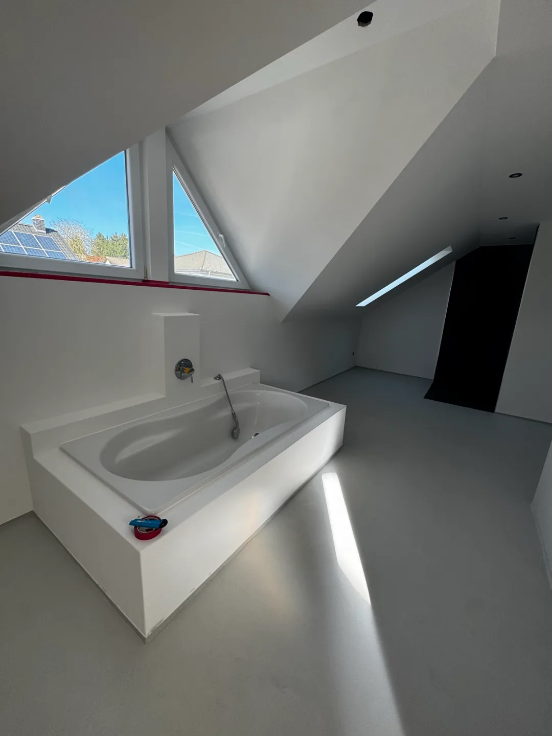 Fugenloses Dachbadezimmer mit verputzter Wanne vor den Giebelfenstern