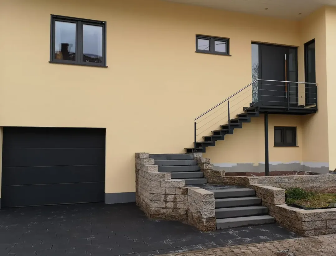 Wohnhaus mit gelb gestrichener Fassade, Außentreppe und Garage in Neunkirchen – Malerbetrieb Mergenthaler